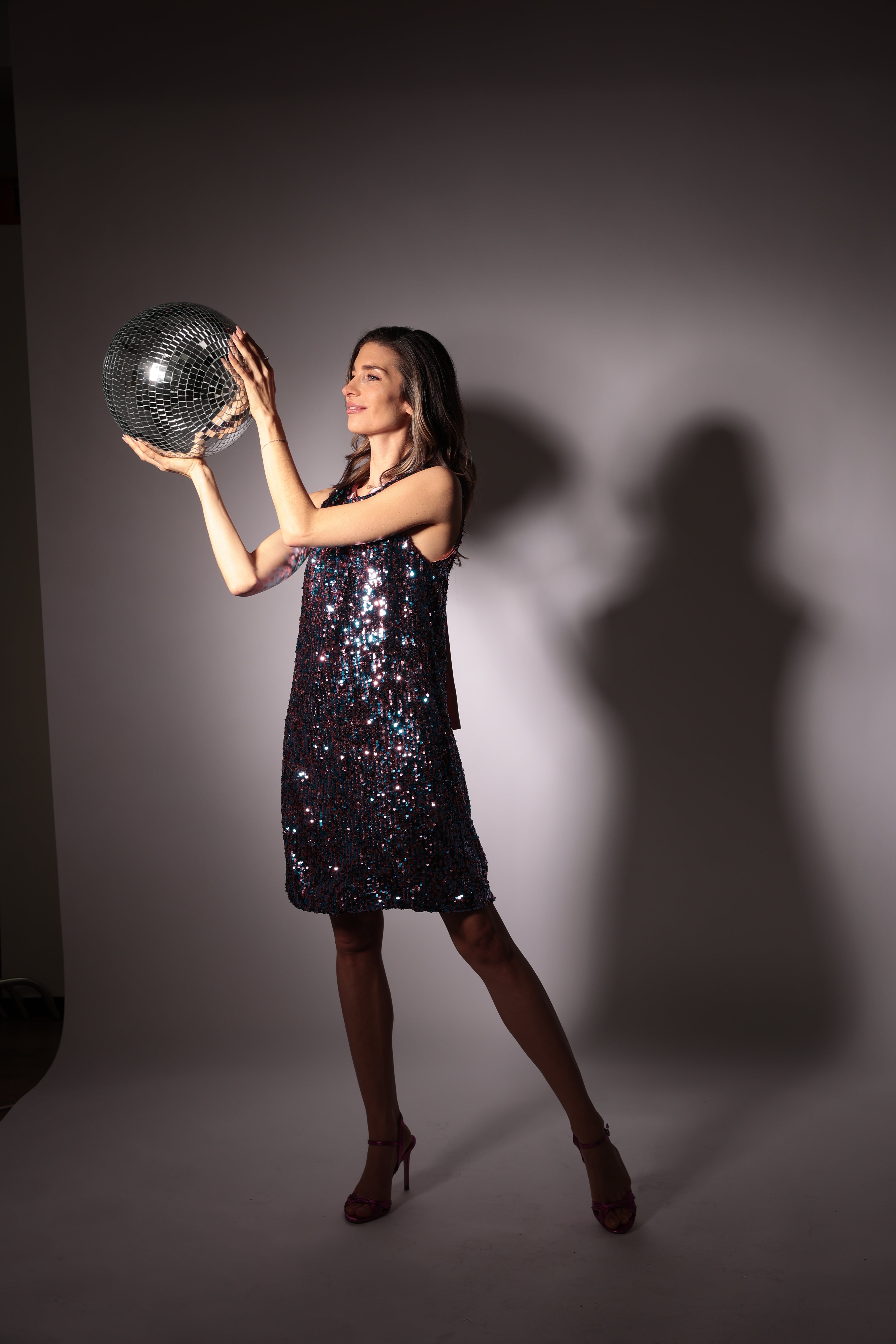 Nettie wearing Ium sequinn shoift dress in pink and blue holding a glitter ball
