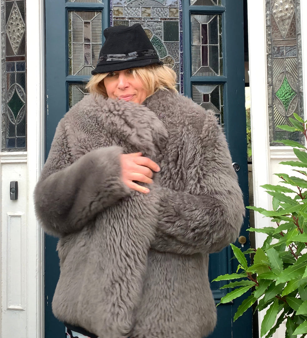 Rebecca walking out of front door in elama long sleeve shirt dress with hat a sheepskin coat