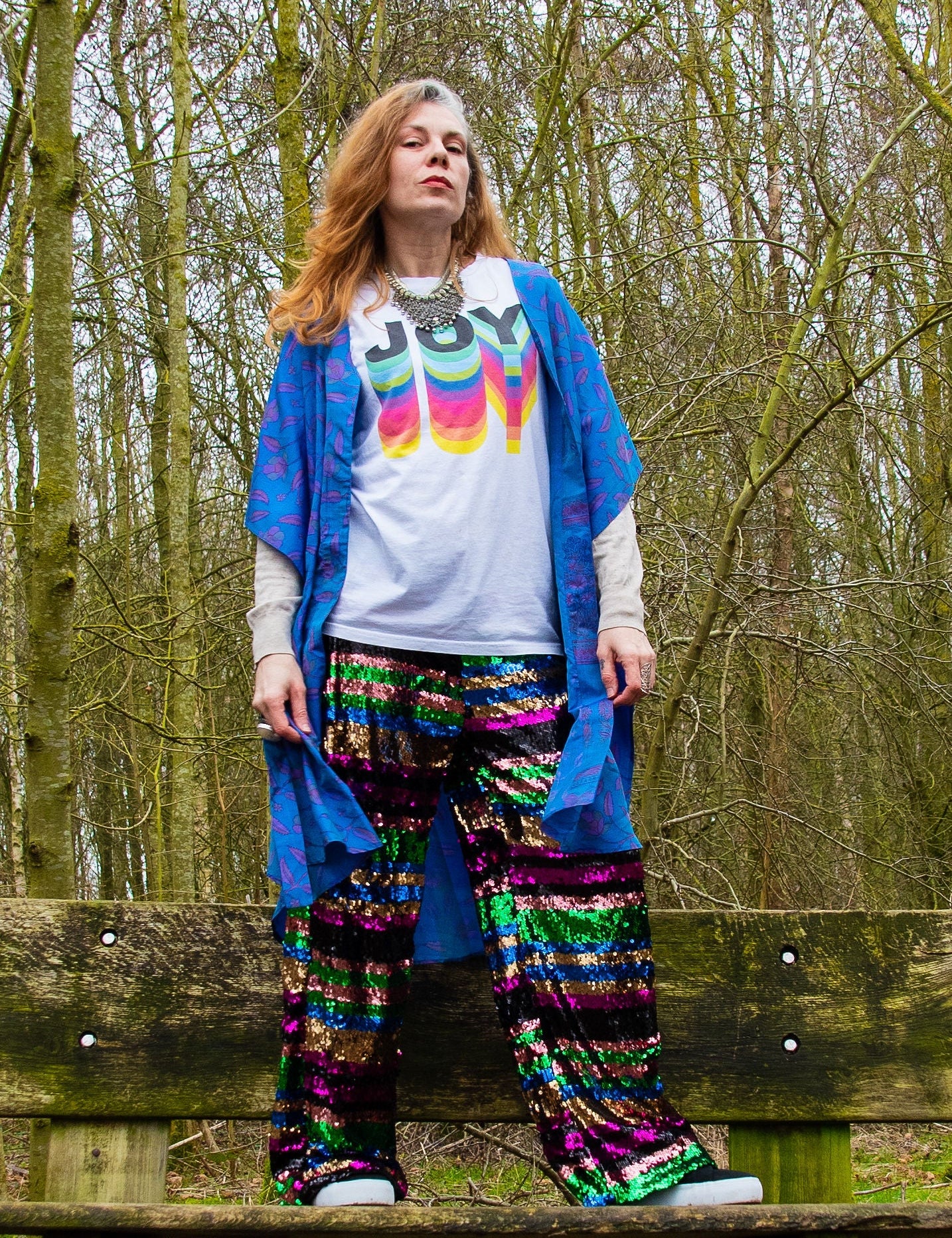 woman standing on bench wearing t shirt saying joy with sequin pants and neem wrap dress