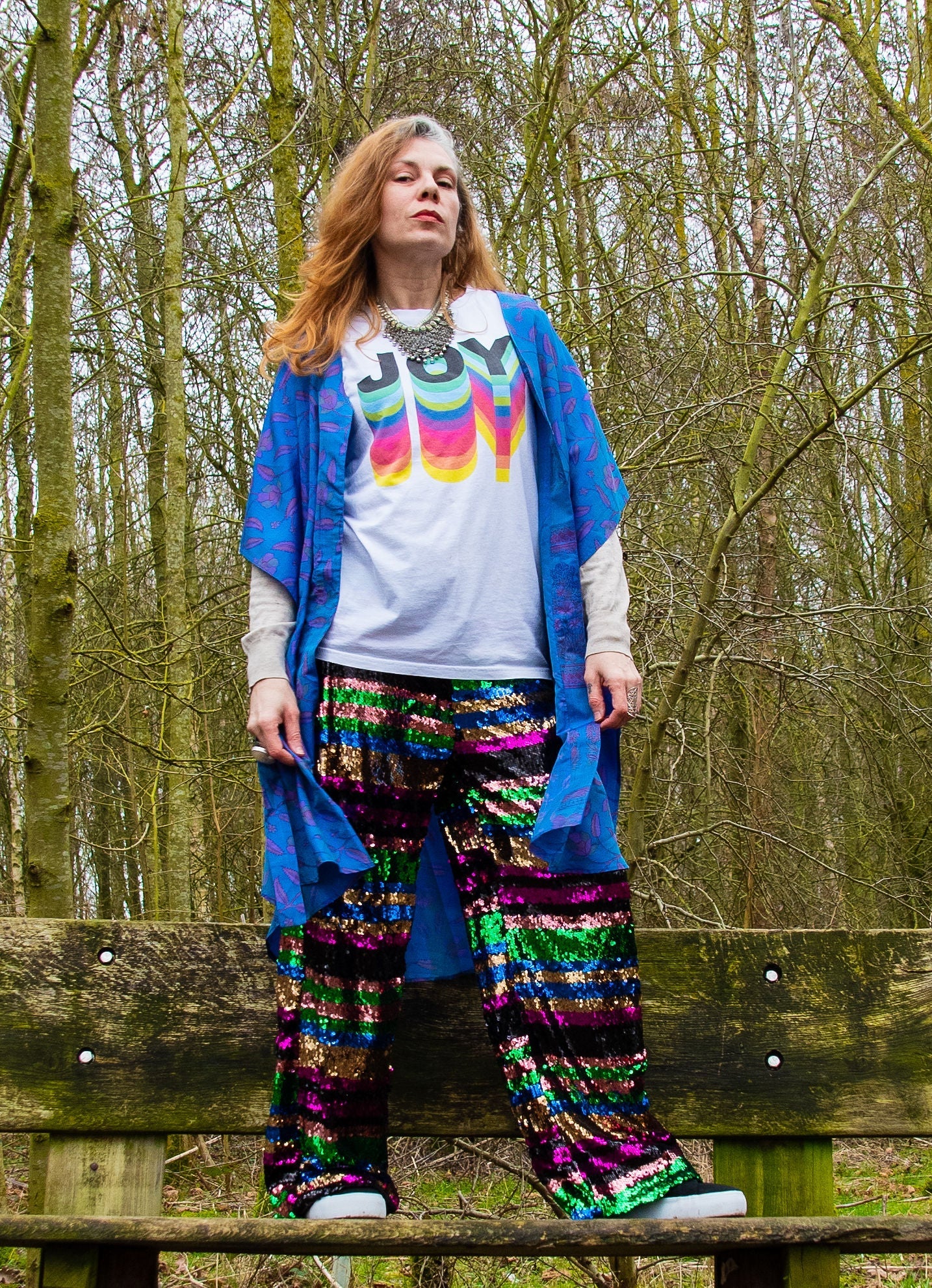 woman standing on bench wearing t shirt saying joy with sequin pants and neem wrap dress