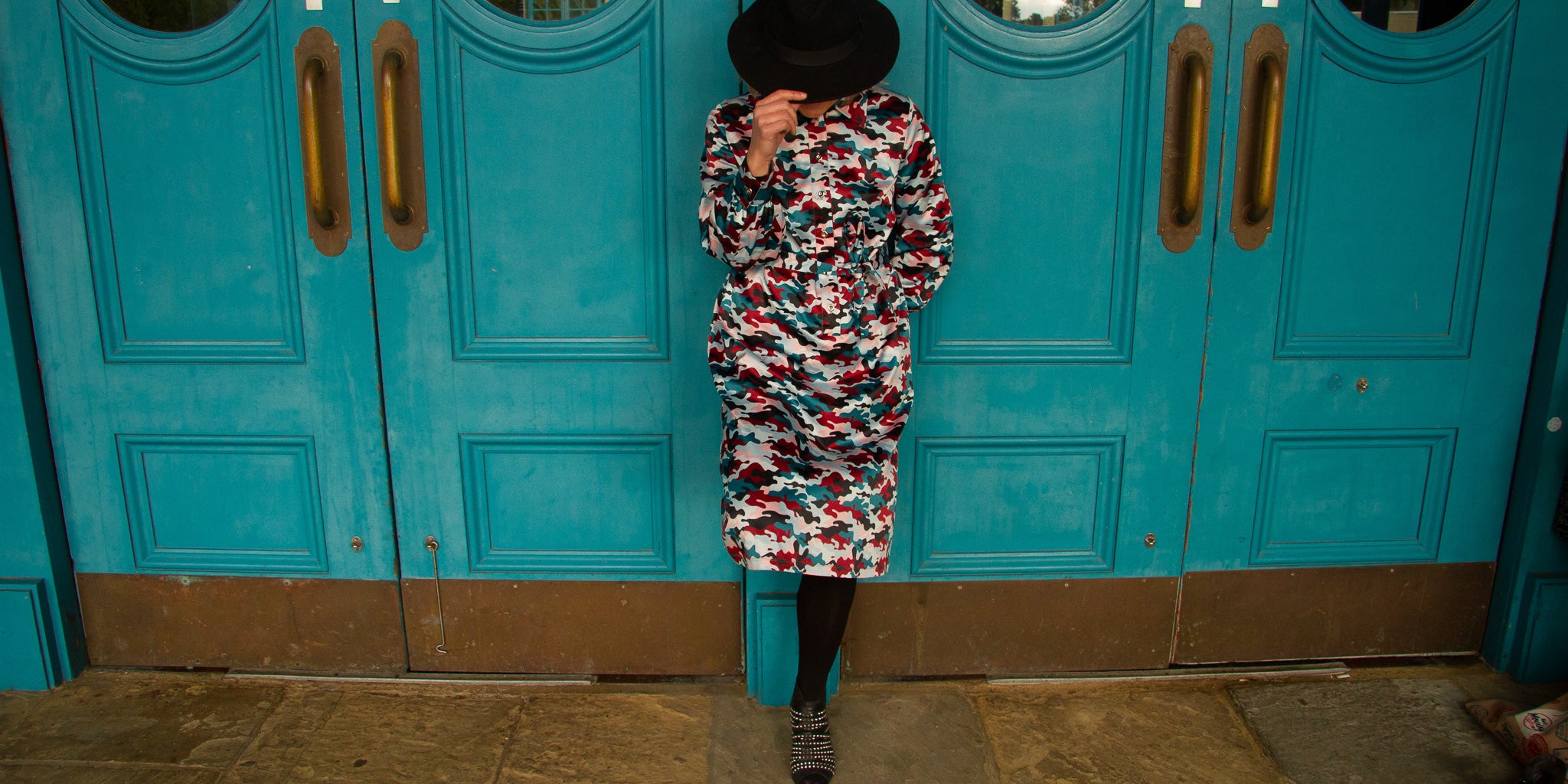 woman in hat wearing elama in sunset camouflage standing in front of blue doors