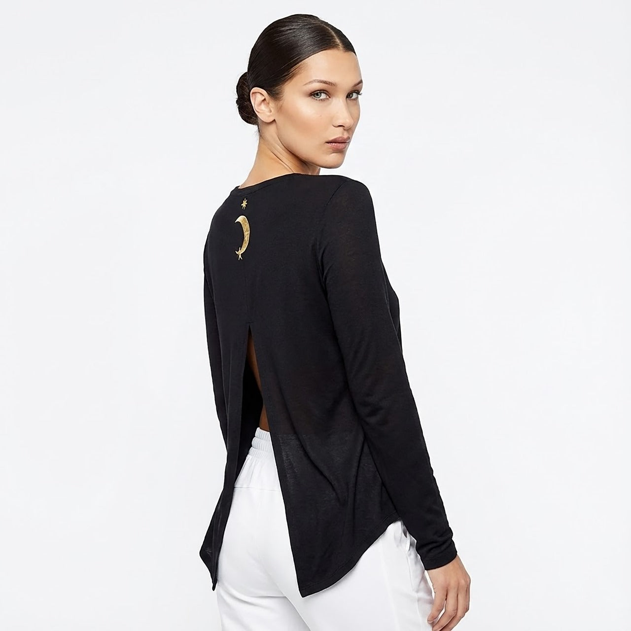 Woman wearing a black long-sleeve top with a unique design on the back against a white background