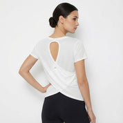 Woman wearing a white t-shirt with an open back design on a plain background