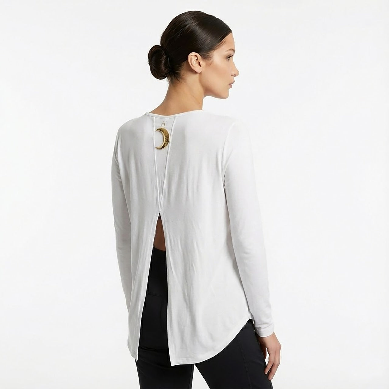 Woman wearing a white blouse with a unique back design on a plain background