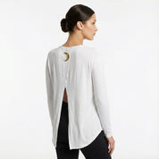 Woman wearing a white blouse with a unique back design on a plain background