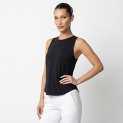 Woman wearing a black sleeveless top and white pants on a light gray background