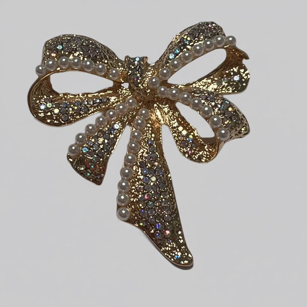 Gold bow-shaped brooch with pearls and gemstones on a light gray background