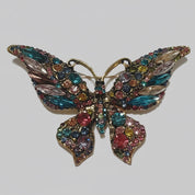 Multicolored butterfly brooch with gemstones on a gray background