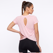 A woman shown from the back wearing a light pink athletic t-shirt with a keyhole cutout and black leggings, set against a plain white studio background.