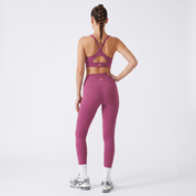 A woman shown from the back wearing a matching mauve-pink sports bra and high-waisted leggings set, paired with white socks and silver sneakers, against a light gray studio background.