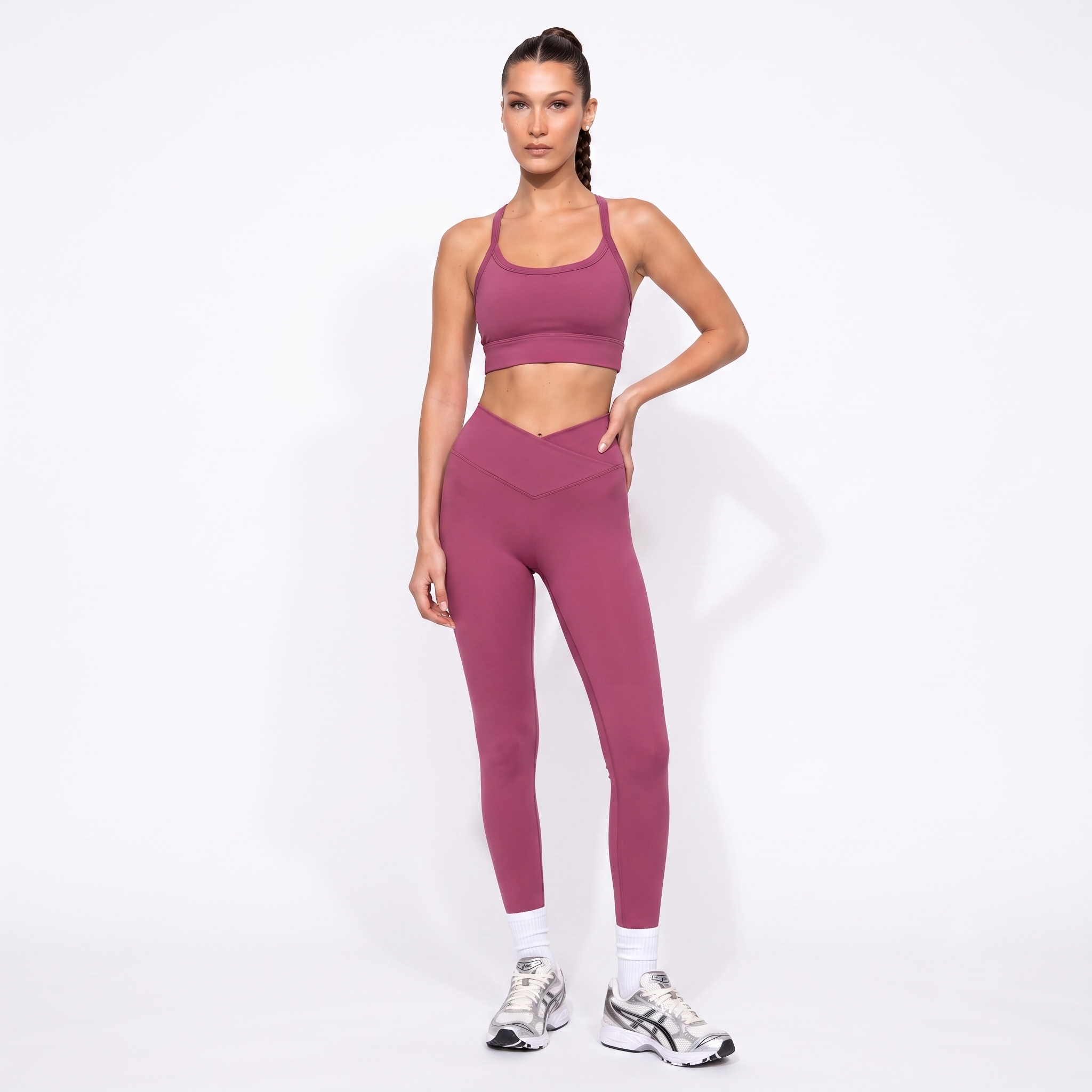 A woman modeling a matching dusty rose activewear set consisting of a sports bra and high-waisted leggings, paired with white socks and athletic sneakers, against a plain white studio background.