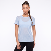 A woman modeling a light blue short-sleeve athletic t-shirt with a sheer circular mesh chest panel, paired with black leggings, against a plain white studio background.