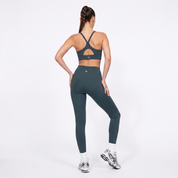 A woman shown from the back wearing a forest green sports bra and matching high-waisted leggings, standing against a clean white studio background.