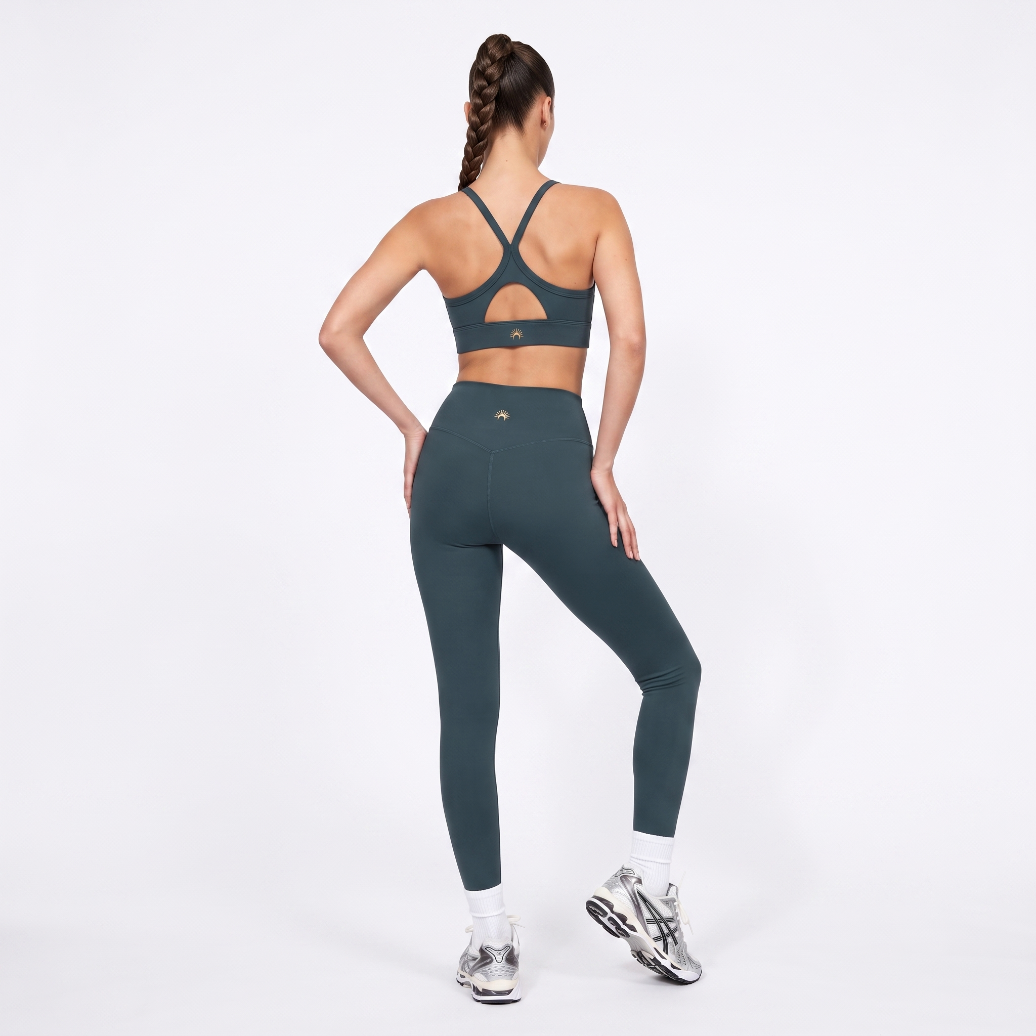 A woman shown from the back wearing a forest green sports bra and matching high-waisted leggings, standing against a clean white studio background.